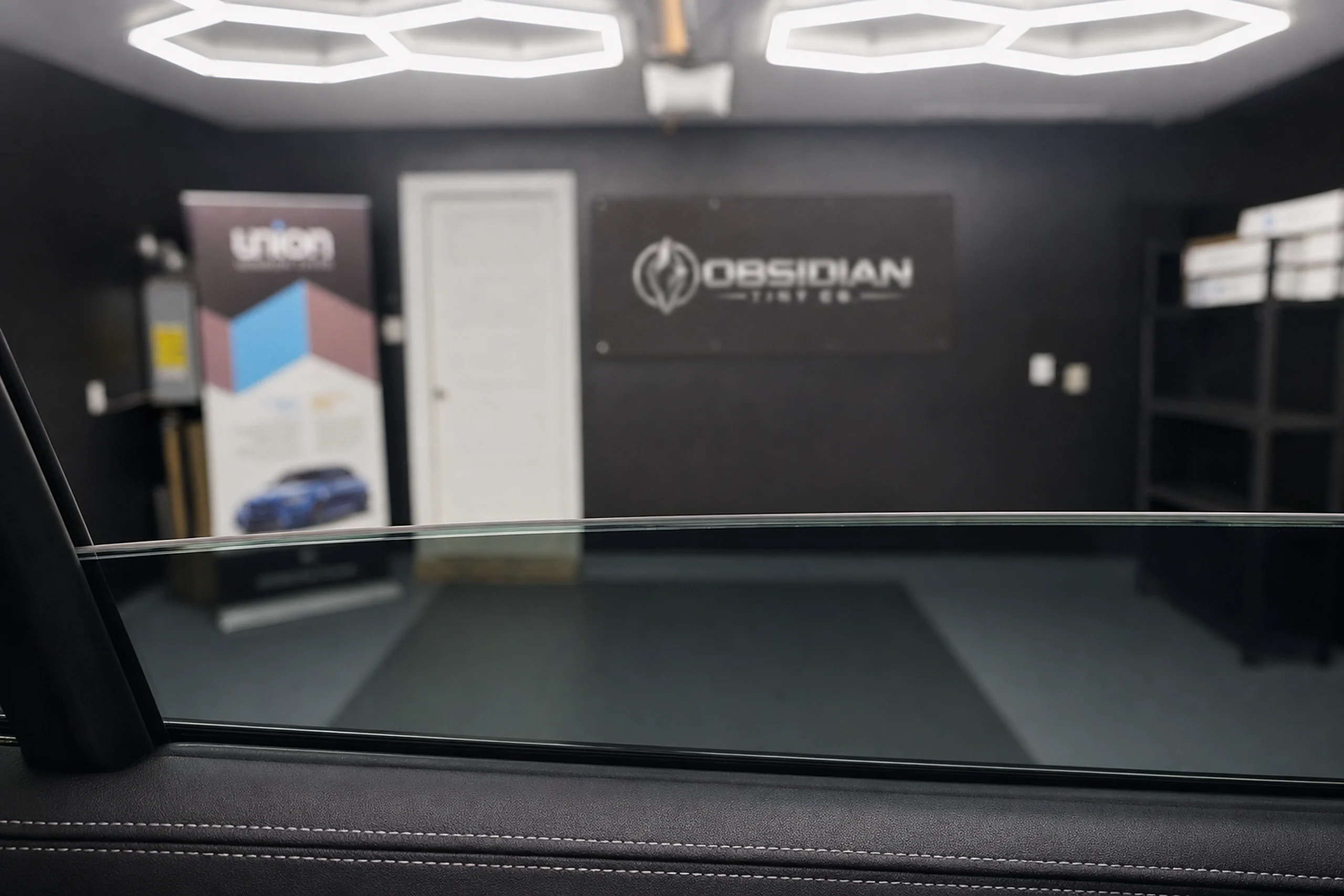 From inside a tinted car, the rear window part way down, the studio soft beyond the glass