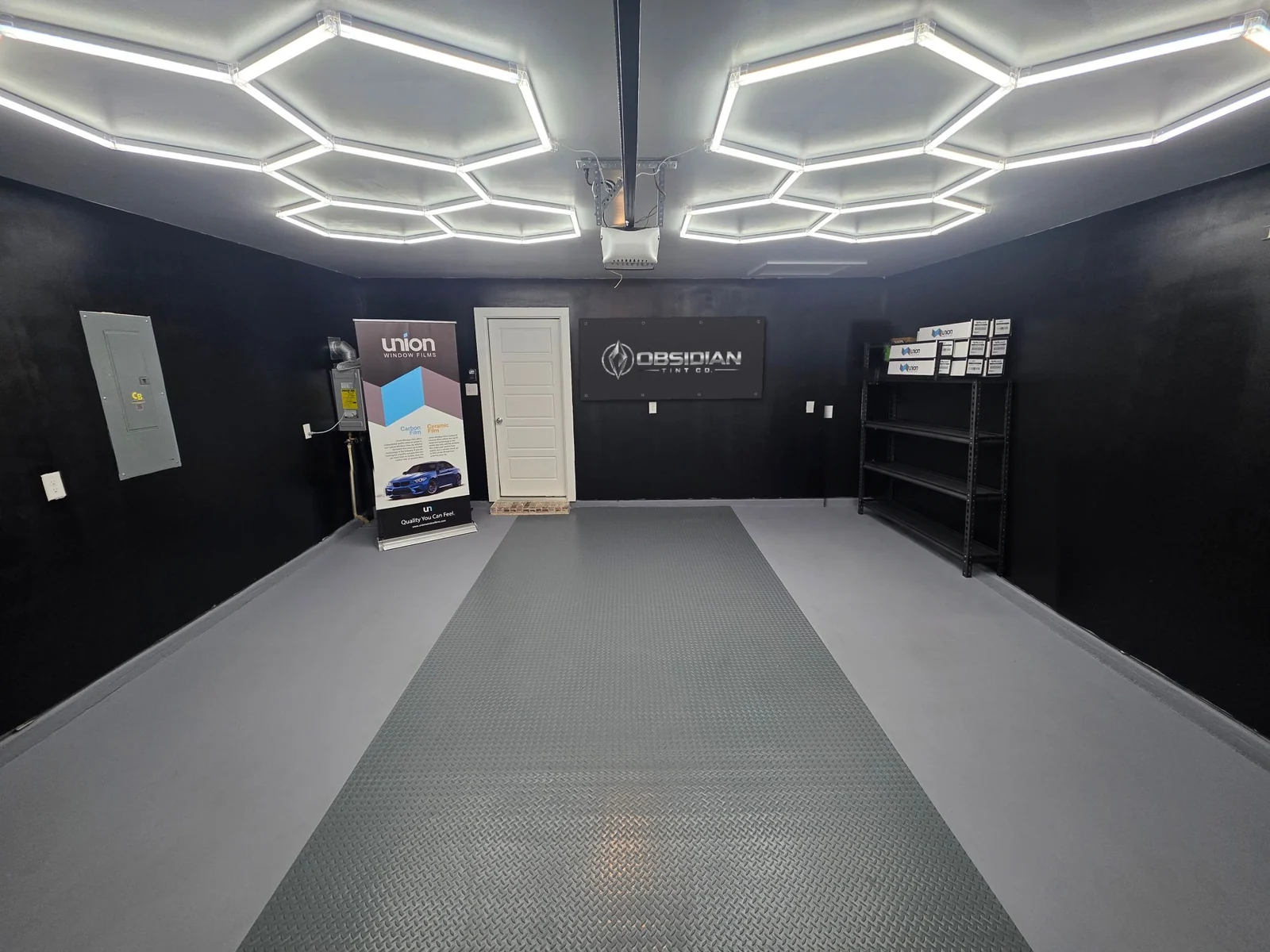 The Obsidian Tint Co home garage studio in Princeton, TX: black walls, hexagon LED lights, a Union Window Films banner and the Obsidian Tint Co banner